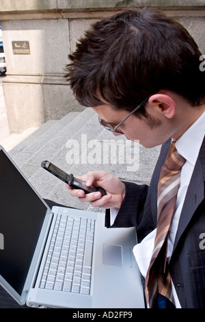 Young businessman uses mobile phone while working on his laptop in the City of London Stock Photo