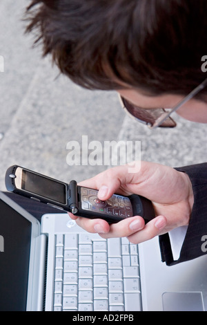 Young businessman uses mobile phone while working on his laptop in the City of London Stock Photo