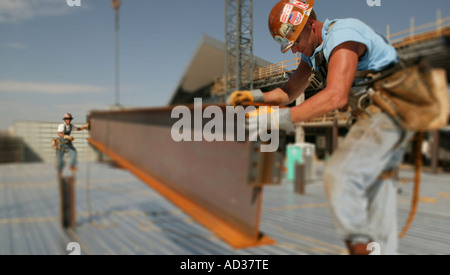 Construction workers guide a steel beam into place with the aid of a ...