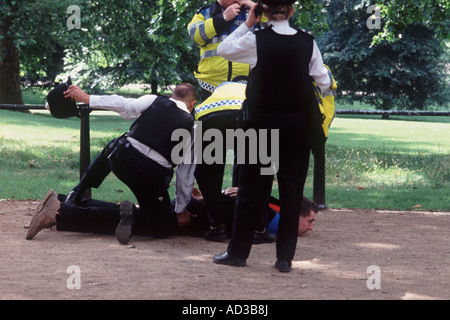 Handcuffed man on ground with chin up surrounded by London Metropolitan police officers, The Mall, St James's Park, London Stock Photo