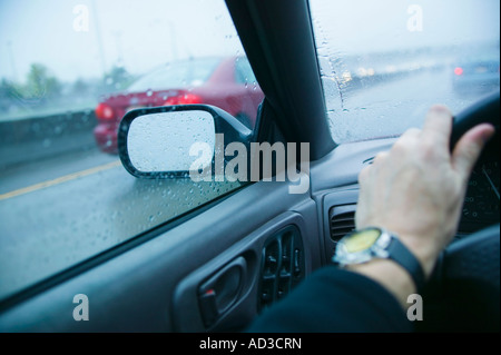 Drivers arm and view through windows on a highway in the rain Stock Photo