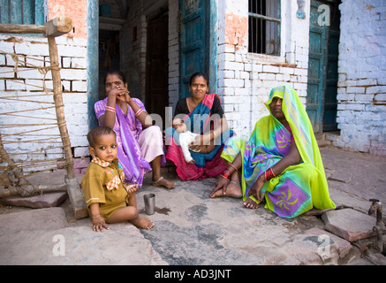 Women wearing brightly coloured saris, seated with their children in the porch of their house. Agra, India. Stock Photo