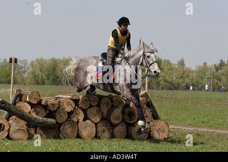 Young rider wearing a riding hat and a body protector galloping on back of an Orlov horse in a meadow Stock Photo