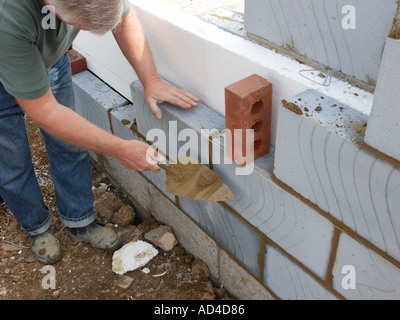 New home under construction with Polystyrene insulation for energy efficient house & bricklayer laying blocks to cavity wall working to string line UK Stock Photo