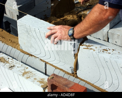 Close up of bricklayer hand & wrist watch placing Celcon insulating block onto cement & sand mortar bed working to string line new cavity wall UK Stock Photo