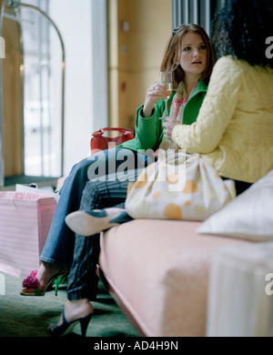 Two friends sitting on a sofa and drinking champagne after a shopping spree Stock Photo