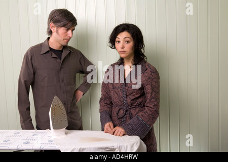 A man and a woman standing next to a burnt shirt on an ironing board Stock Photo