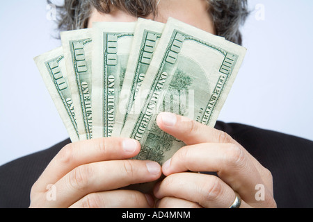 A businessman holding a fan of hundred dollar bills in front of his face Stock Photo