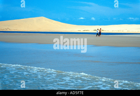 A couple walking on Pansy Shell Island with giant sand dunes of Bazaruto Island Ilha do Bazaruto behind them Bazaruto Archip Stock Photo