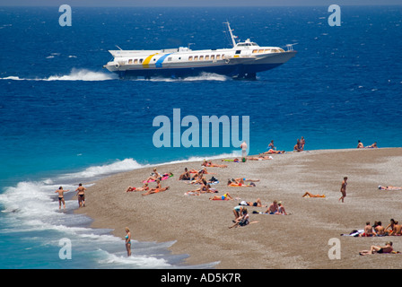 Horizontal aerial view of holidaymakers sunbathing on the beach and swimming in the sea with a hydrofoil passenger ferry zooming Stock Photo