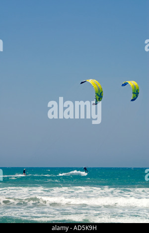 Vertical wide angle of two kitesurfers performing dramatic acrobatic jumps off the tops of the waves on a sunny day. Stock Photo