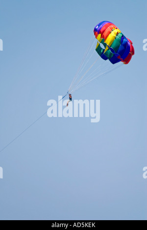Vertical close up of a young woman para-sailing, para sailing, with a multi-coloured parachute against a bright blue sky. Stock Photo