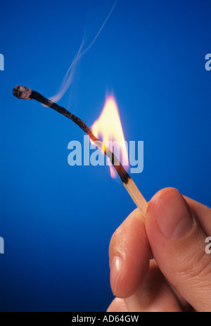 Close-up of man's hand holding a lit wooden match against a blue background Stock Photo