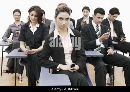 Business executives sitting on chairs holding mobile phones Stock Photo