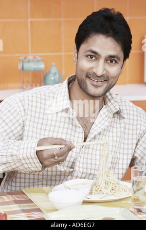 Portrait of a mid adult man holding noodles with a pair of chopsticks Stock Photo