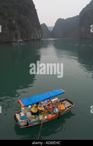 Northeast Vietnam Halong Bay Woman paddling a floating grocery on a dingy with typical rock formation in bkgd Stock Photo