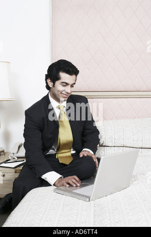 Businessman sitting on the bed using a laptop Stock Photo