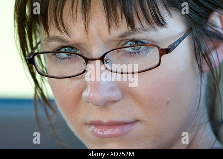 A caucasian, brunette woman with bangs and glasses looks at the camera. Stock Photo