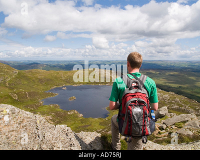 Young man walker carrying a rucksack looking at view to Llyn y Foel lake from Moel Siabod Daear Ddu ridge in Snowdonia Wales UK Stock Photo