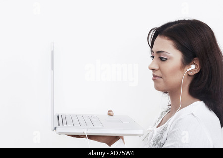 Side profile of a young woman wearing headphones holding a laptop Stock Photo