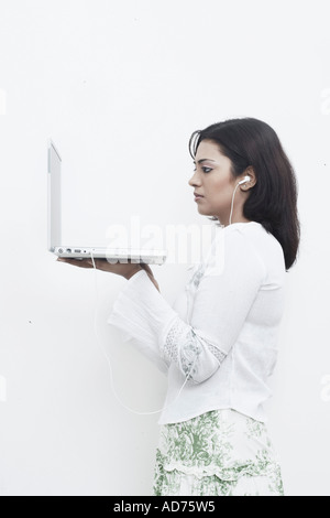 Side profile of a young woman wearing headphones holding a laptop Stock Photo