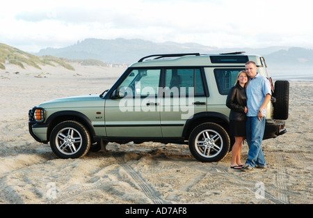 Young couple standing on beach in front of SUV Stock Photo
