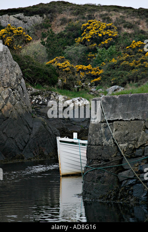 Safe Harbour: A white wooden boat peeks out from behind a dark grey seaweed encrusted wharf that matches the rock wall behind Stock Photo