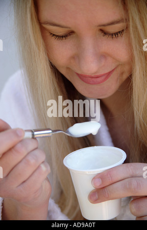 Young blond woman eating pure yogurt, close up Stock Photo