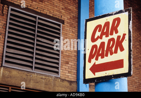 Peeling painted sign with arrow pointing to Car park entrance with a dented air vent high brick wall and stained concrete Stock Photo