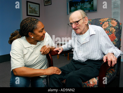 Member of care staff interacting with elderly man at care home for people suffering from dementia, London, UK.
