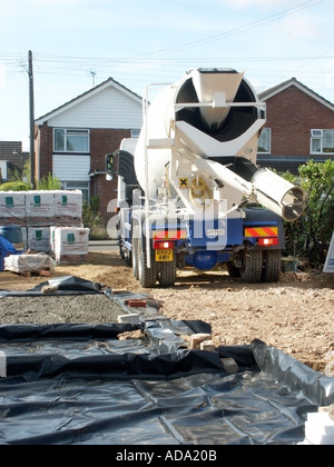 Concrete cement mixer delivery lorry truck reverse onto construction building site to pour more concrete on plastic damp proof membrane England UK Stock Photo