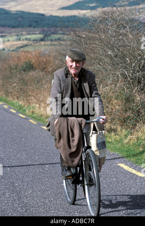 elderly man cycling along a narrow irish country lane, old man with cap jacket, and overcoast thrown over handle bars Stock Photo