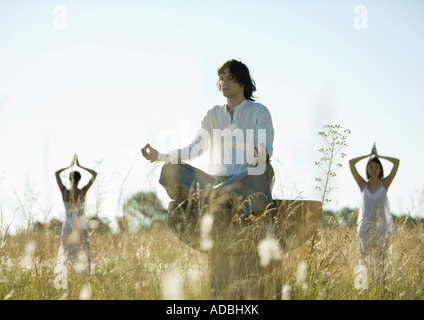 Young male and females doing yoga in field Stock Photo