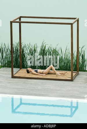 Woman wearing bikini, lying on back in square structure between lake and pool Stock Photo