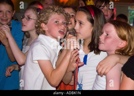 Horizontal close up of a group of female children around several microphones enjoying themselves singing karaoke at a party Stock Photo