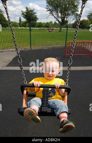 Vertical close up portrait of a 16 month old baby boy having great fun being pushed on the swings in a park Stock Photo