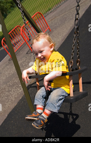 Vertical close up portrait of a 16 month old baby boy having great fun being pushed on the swings in a park Stock Photo