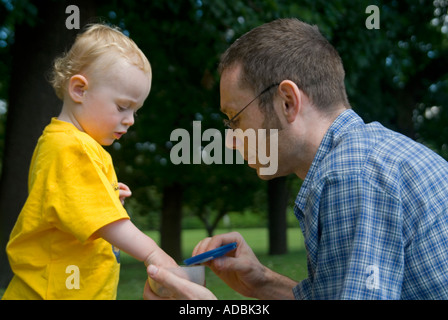 Horizontal close up portrait of a 16 month old baby boy with his dad sharing out raisins from a plastic tub as a reward Stock Photo