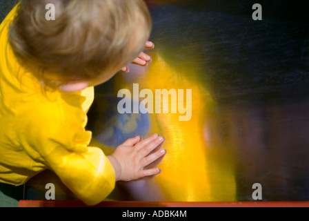 Horizontal portrait of a 16 month old baby boy looking at his reflection in a metallic slide, in the park on a sunny day. Stock Photo