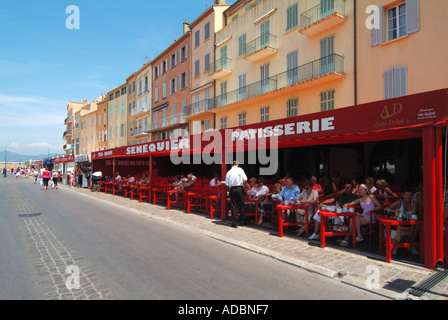 Senequier Patisserie and bar waiter carrying drinks tray walking along waterfront serving customers sitting in shade at St Tropez South of France Stock Photo