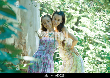 Two young women wearing sundresses, standing in forest, taking photo of selves with digital camera Stock Photo