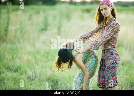 Young women in field, one bending over while the other holds her back Stock Photo