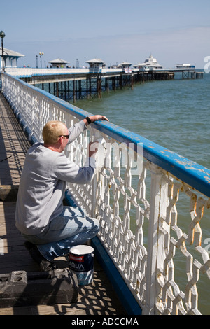 Painting metal railings white on Llandudno pier Wales UK Stock Photo