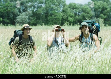 Three hikers standing in field, one looking through binoculars Stock Photo