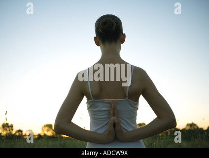 Woman doing yoga pose, hands clasped behind back, at sunset Stock Photo