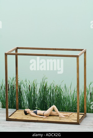 Woman wearing bikini, lying on back in square structure near lake Stock Photo