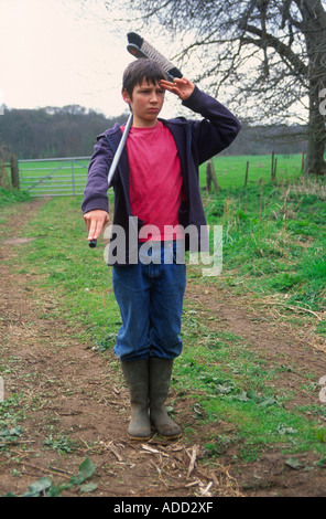 Young boy using a broom and pretending to be a soldier standing to attention and saluting Stock Photo