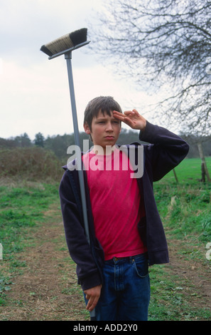 Young boy using a broom and pretending to be a soldier standing to attention and saluting Stock Photo