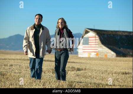 Man and women smiling walking through cut grass fields in Fall with barn and american flag Colorado Stock Photo