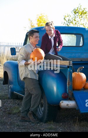 Middle aged couple unloads pumpkins from old blue pickup truck while having fun vertical Stock Photo